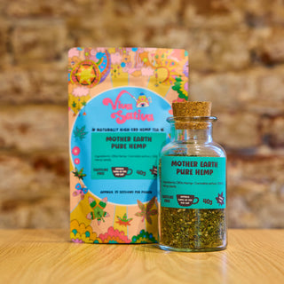 Viva Sativa Mother Earth Pure Hemp CBDa tea in a glass jar with cork lid, alongside its colourful packaging on a wooden table at Camden Tea Bar.